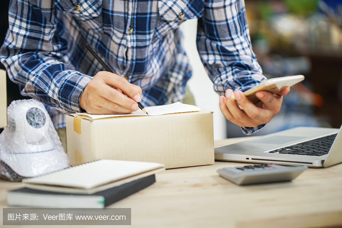 年輕的創業小企業主在工作場所的盒子里裝攝像頭閉路電視。自由職業者銷售者準備產品的包裝過程在家里。網絡銷售,網絡營銷,